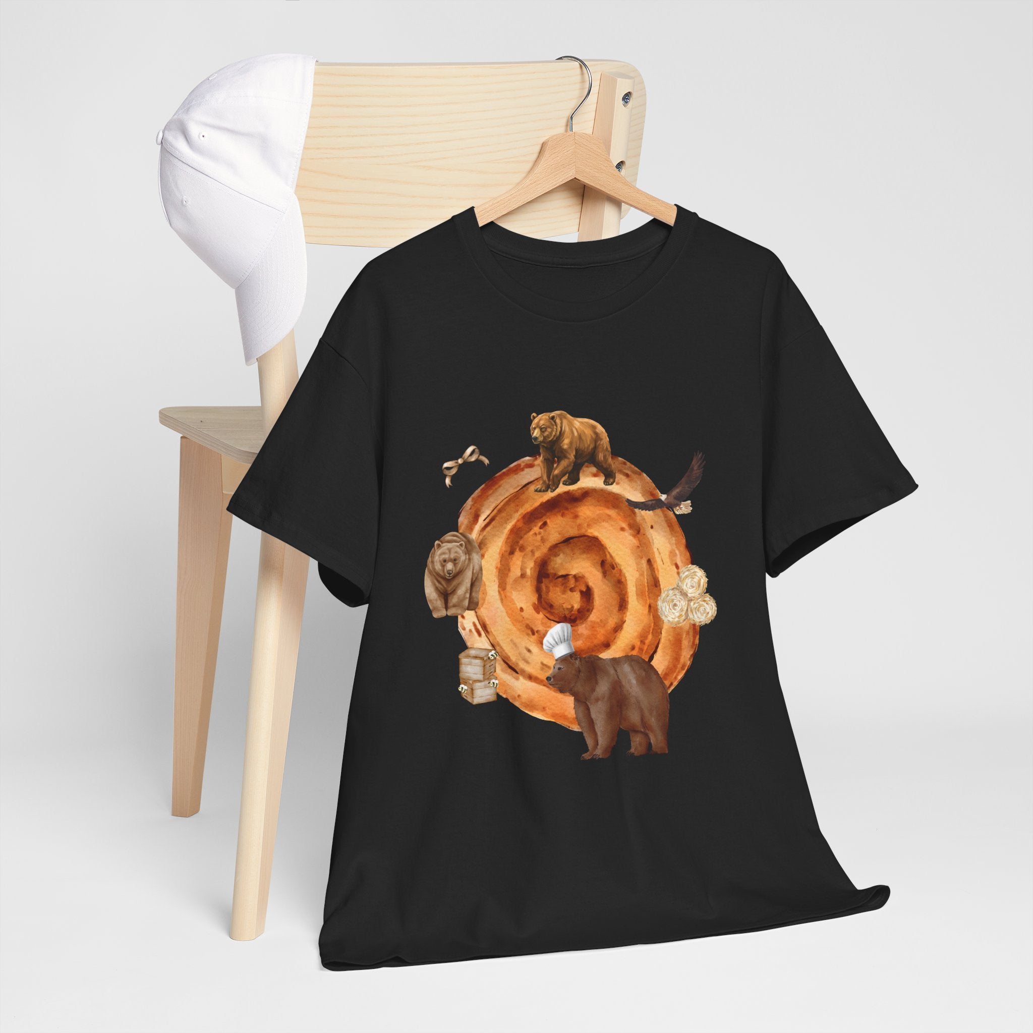 A black t-shirt hanging on a chair, featuring a graphic design of a cinnamon roll surrounded by several hungry bears.