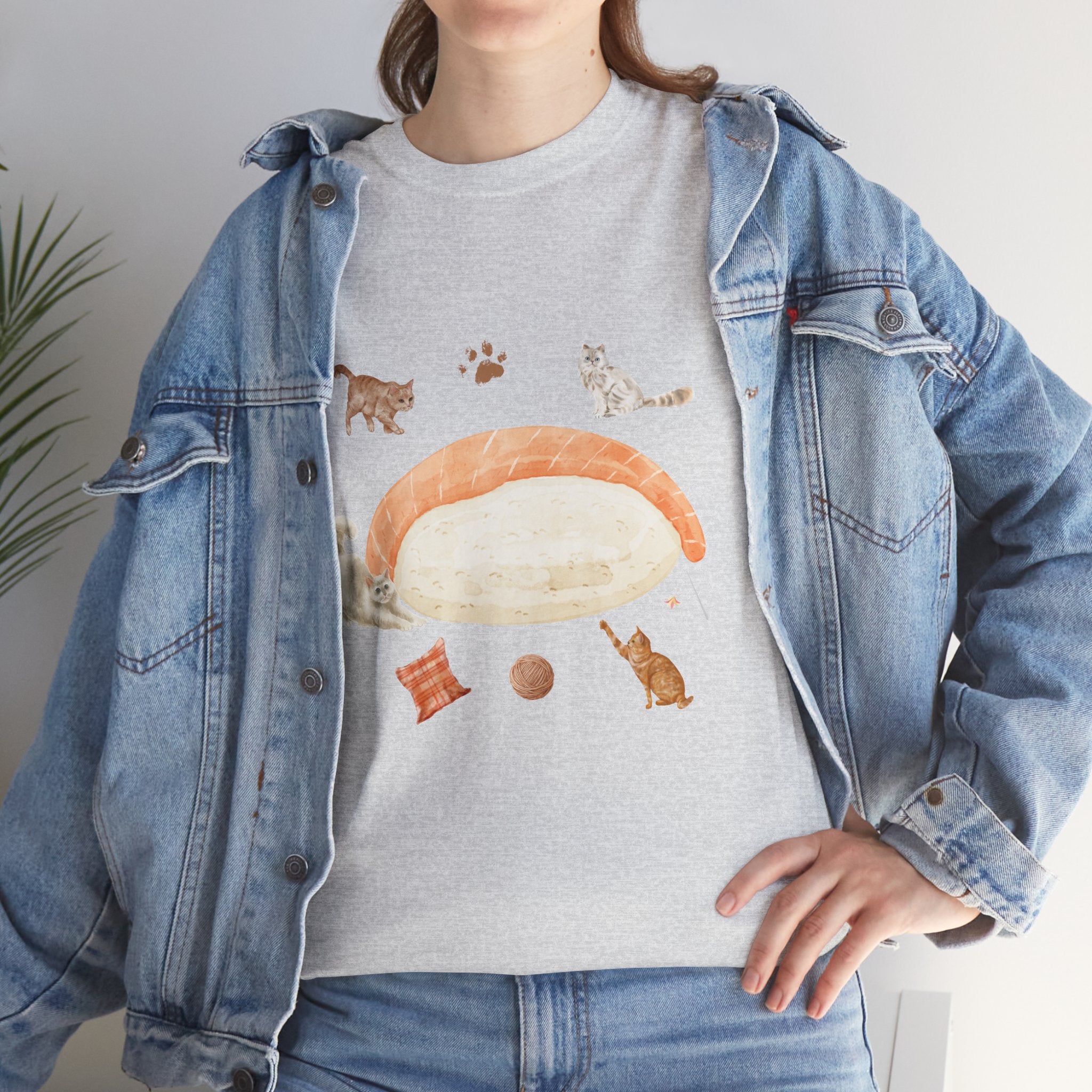 A girl wearing a denim jacket over a grey t-shirt featuring a colorful design of a piece of nigiri sushi surrounded by a circle of cats, yarn balls, and cushions.