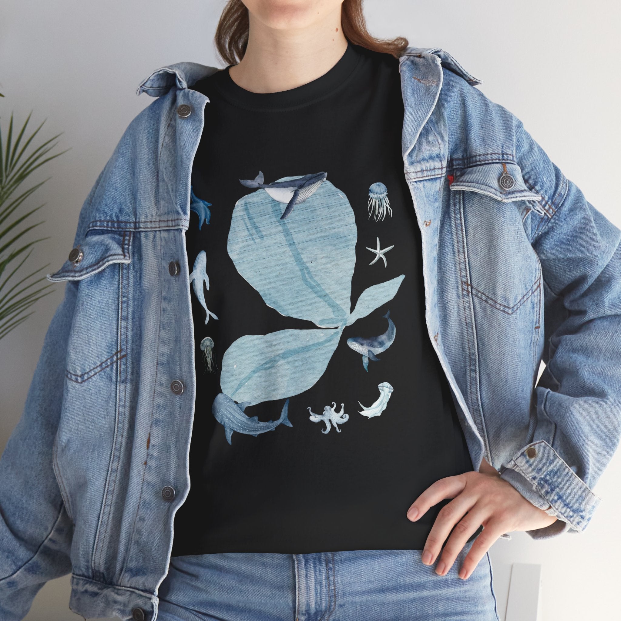 A girl wearing a denim jacket over a black t-shirt featuring a colorful design of a blue bloom surrounded by whales, jellyfish, and starfish.