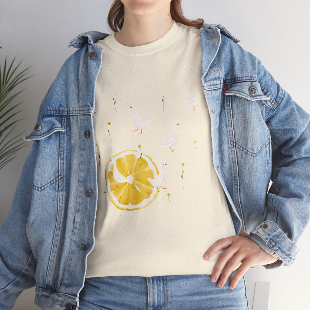 A girl wearing a denim jacket over a beige t-shirt featuring a colorful design of white ducks covering the shirt with a juicy lemon in the bottom-left corner.