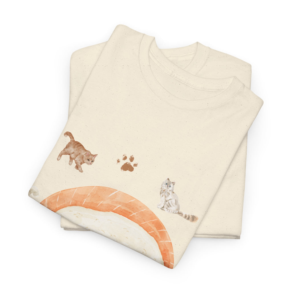 A folded beige t-shirt featuring a graphic design of a piece of nigiri sushi surrounded by a circle of cats, yarn balls, and cushions.