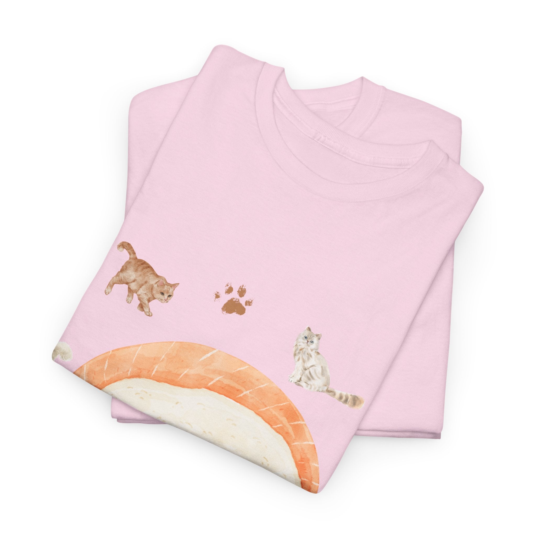 A folded pink t-shirt featuring a graphic design of a piece of nigiri sushi surrounded by a circle of cats, yarn balls, and cushions.