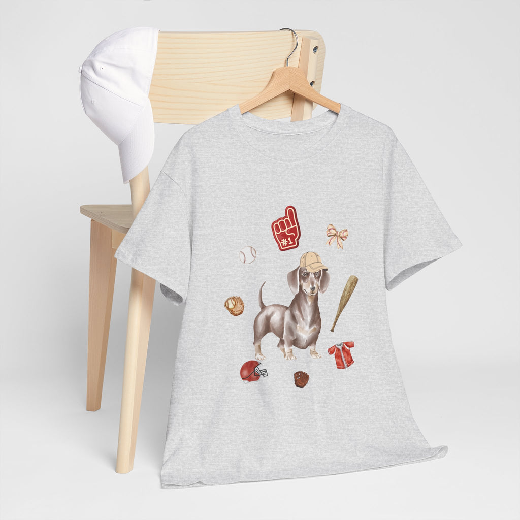 A grey t-shirt hanging on a chair, featuring a graphic design of a dog in a baseball hat surrounded by a circle of balls, bats, and helmets.