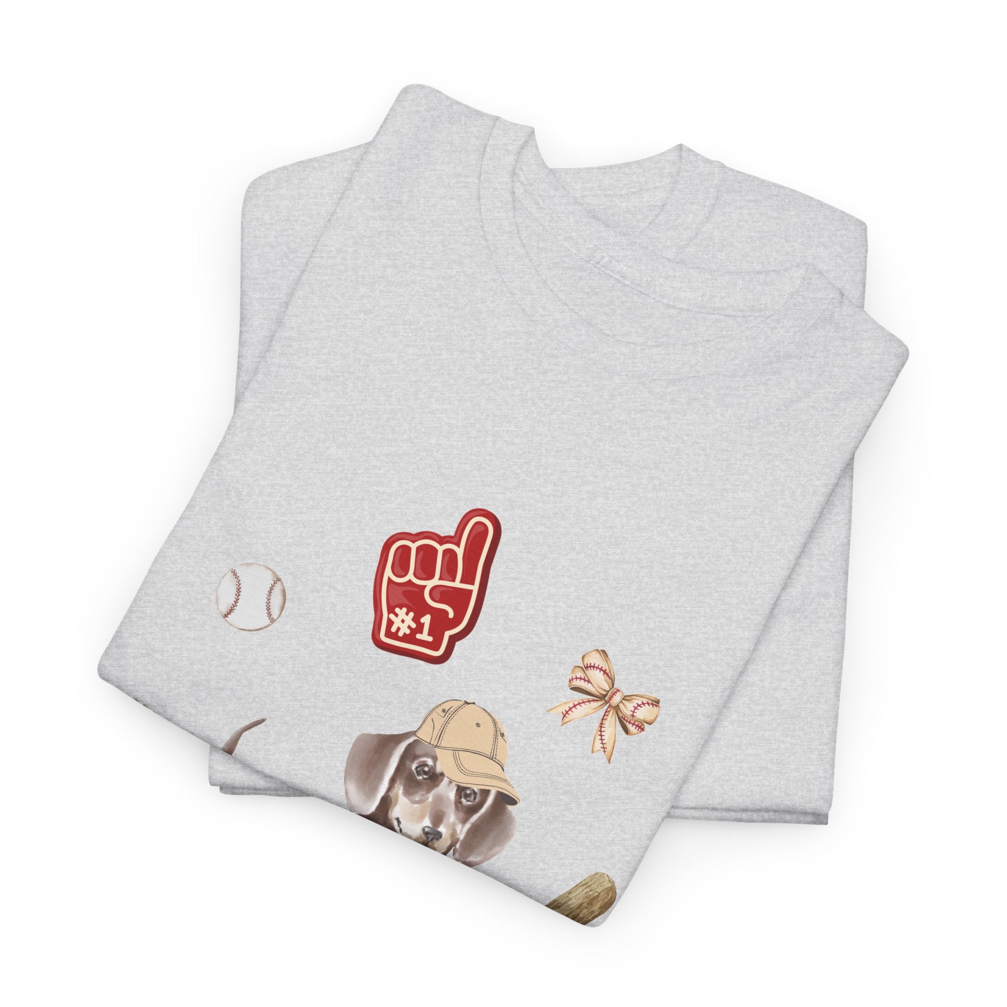 A folded grey t-shirt featuring a graphic design of a dog in a baseball hat surrounded by a circle of balls, bats, and helmets.