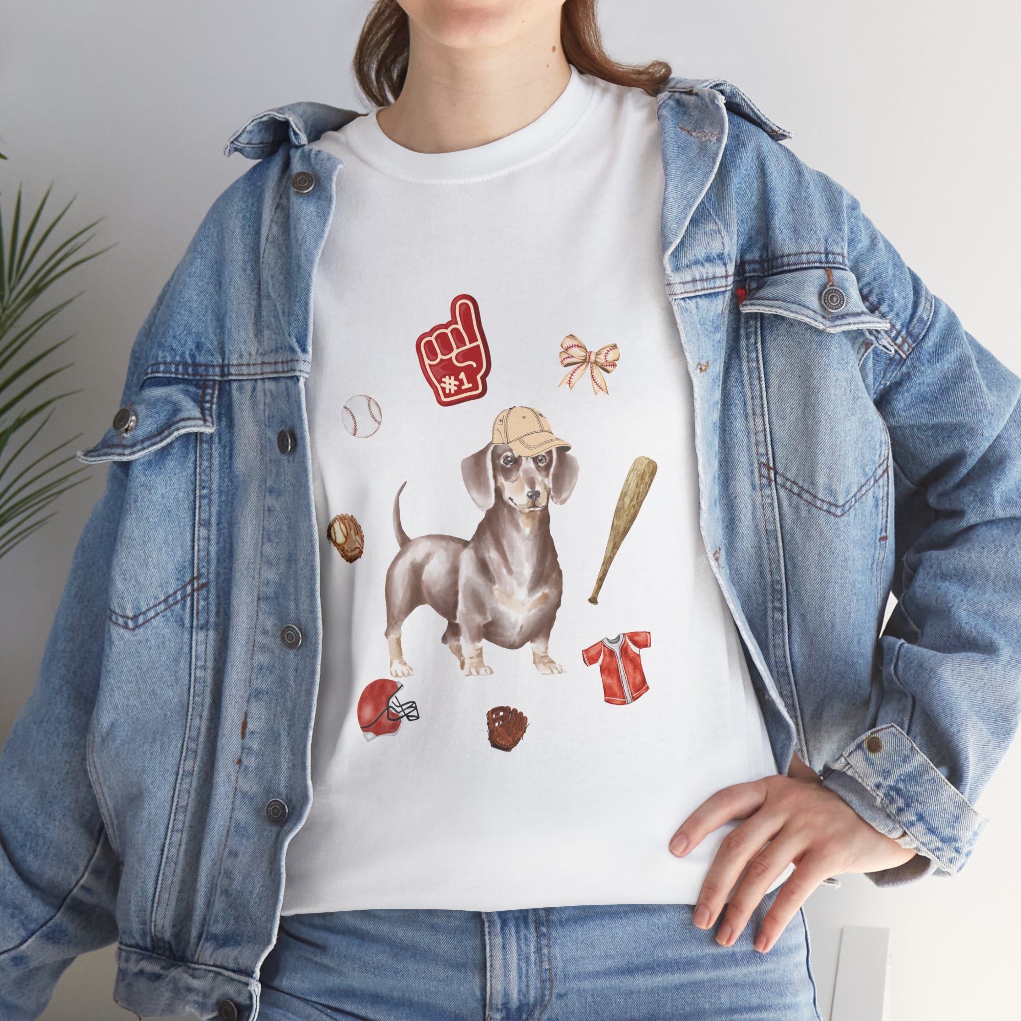 A girl wearing a denim jacket over a white t-shirt featuring a colorful design of a dog in a baseball hat surrounded by a circle of balls, bats, and helmets.