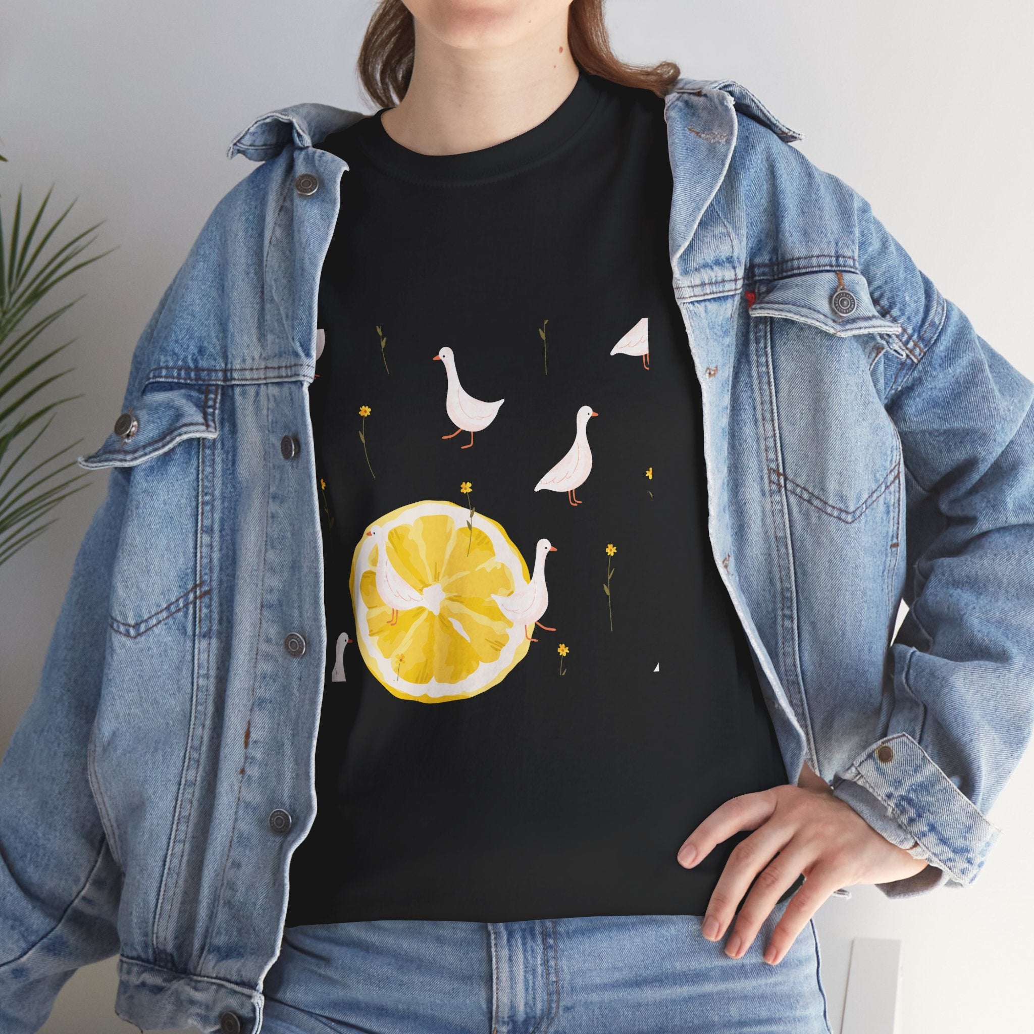 A girl wearing a denim jacket over a black t-shirt featuring a colorful design of white ducks covering the shirt with a juicy lemon in the bottom-left corner.