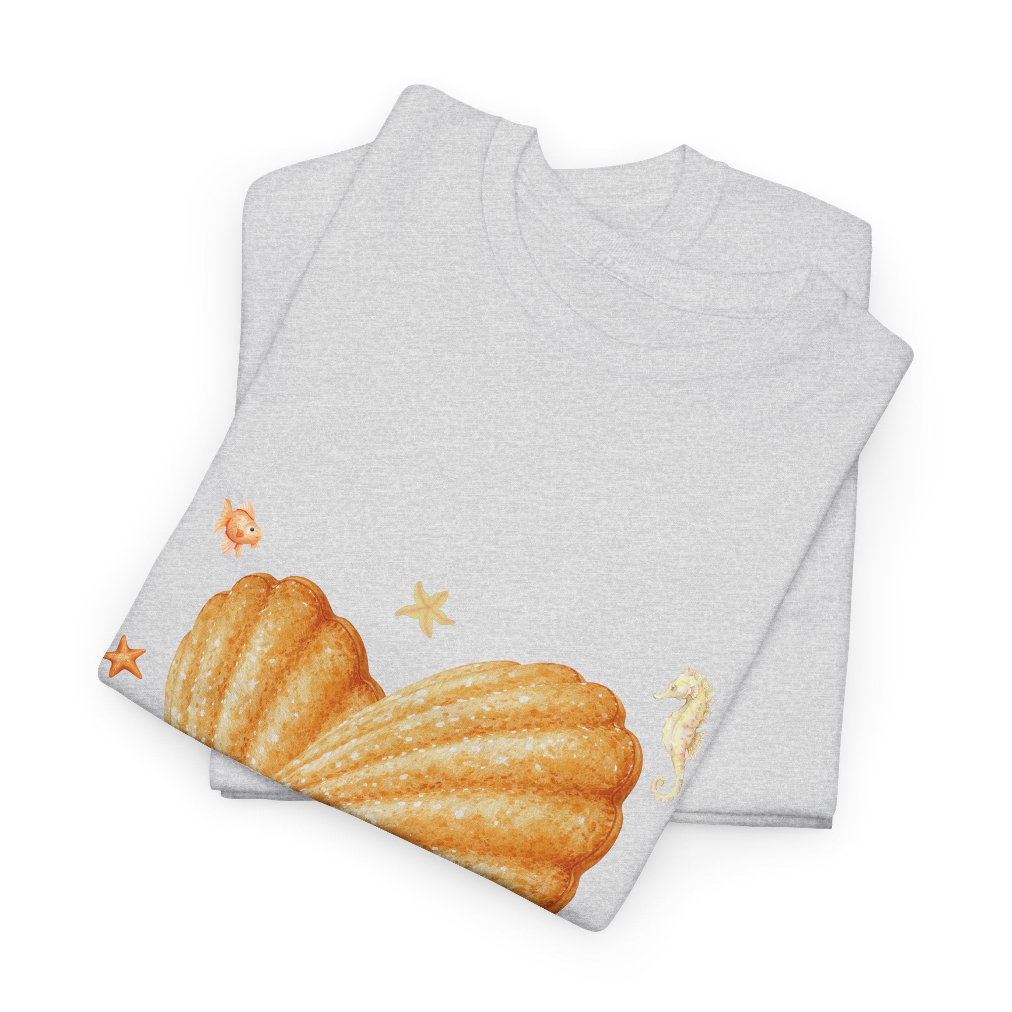 A folded white t-shirt featuring a graphic design of a heart-shaped madeleine surrounded by yellow tropical fish, starfish, seahorses, and coral.