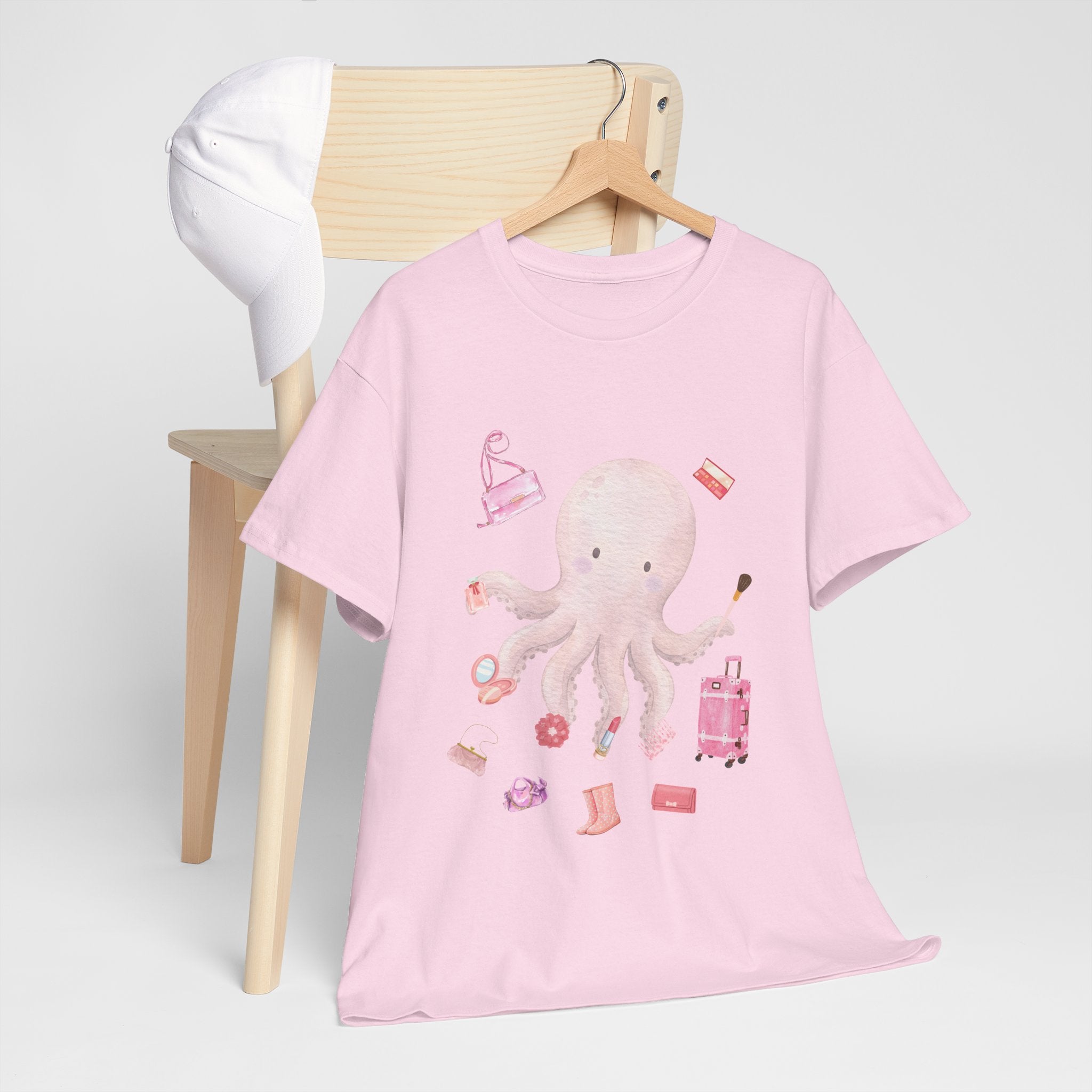 A pink t-shirt hanging on a chair, featuring a graphic design of a pink octopus multitasking its tentacles to apply lipstick, brush on makeup, and juggle beauty accessories.