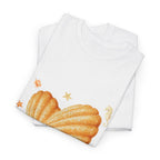 A folded white t-shirt featuring a graphic design of a heart-shaped madeleine surrounded by yellow tropical fish, starfish, seahorses, and coral.