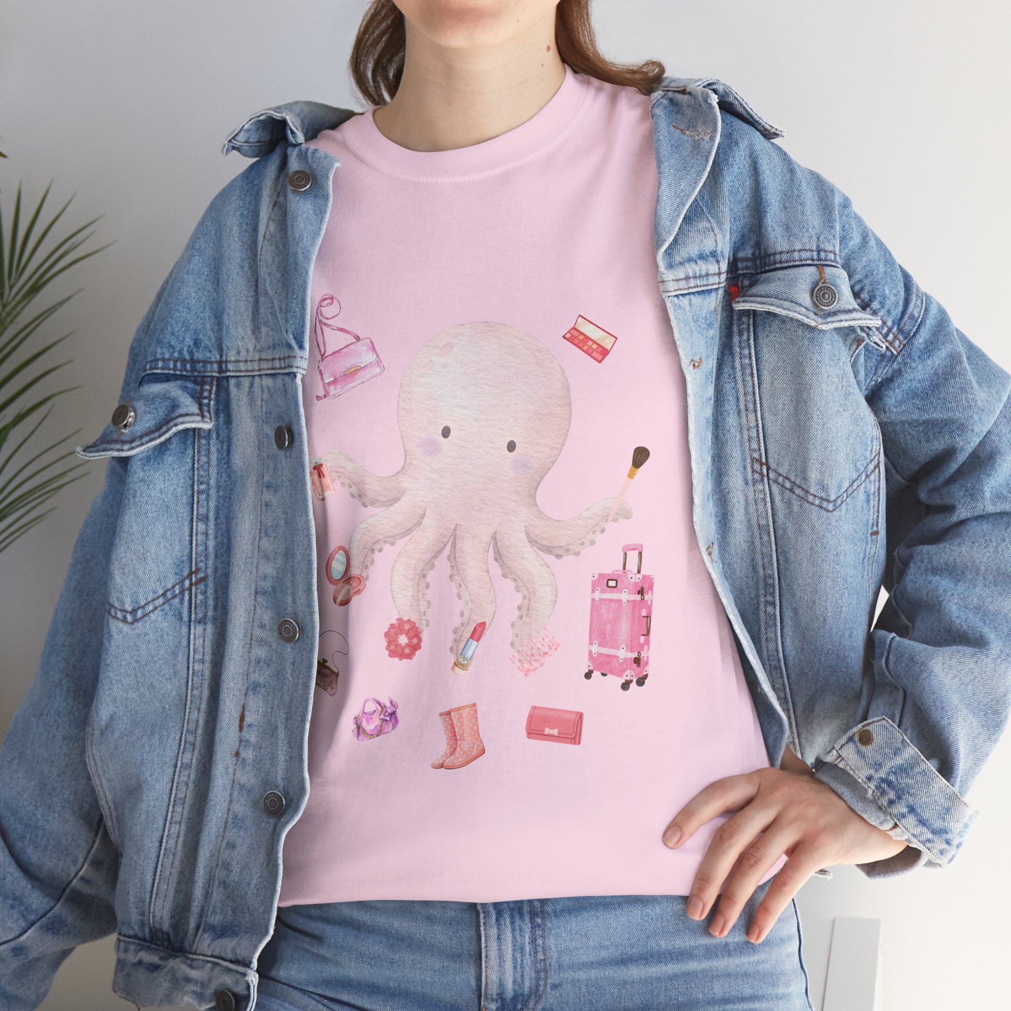 A girl wearing a denim jacket over a pink t-shirt featuring a colorful design of a pink octopus multitasking its tentacles to apply lipstick, brush on makeup, and juggle beauty accessories.