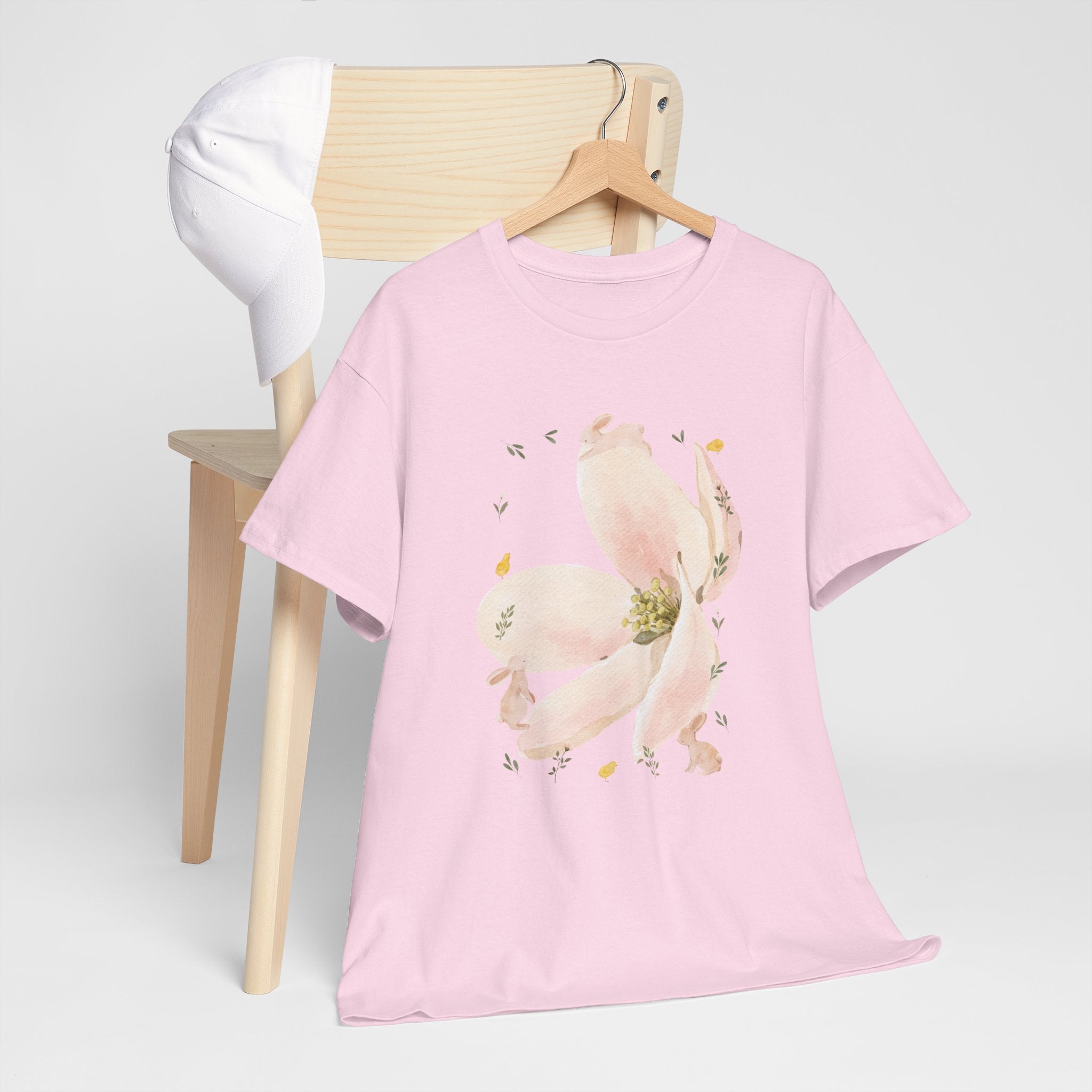 A pink t-shirt hanging on a chair, featuring a graphic design of a pink bloom surrounded by bunnies in various poses.