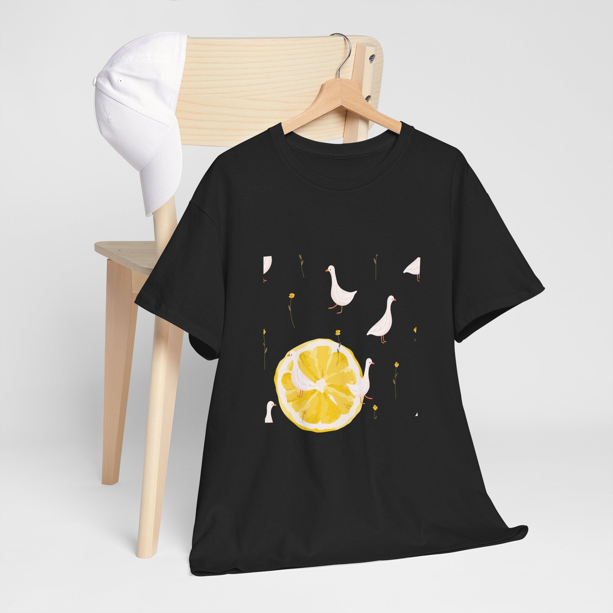 A black t-shirt hanging on a chair, featuring a graphic design of white ducks across the whole shirt and a juicy lemon in the bottom-left corner.