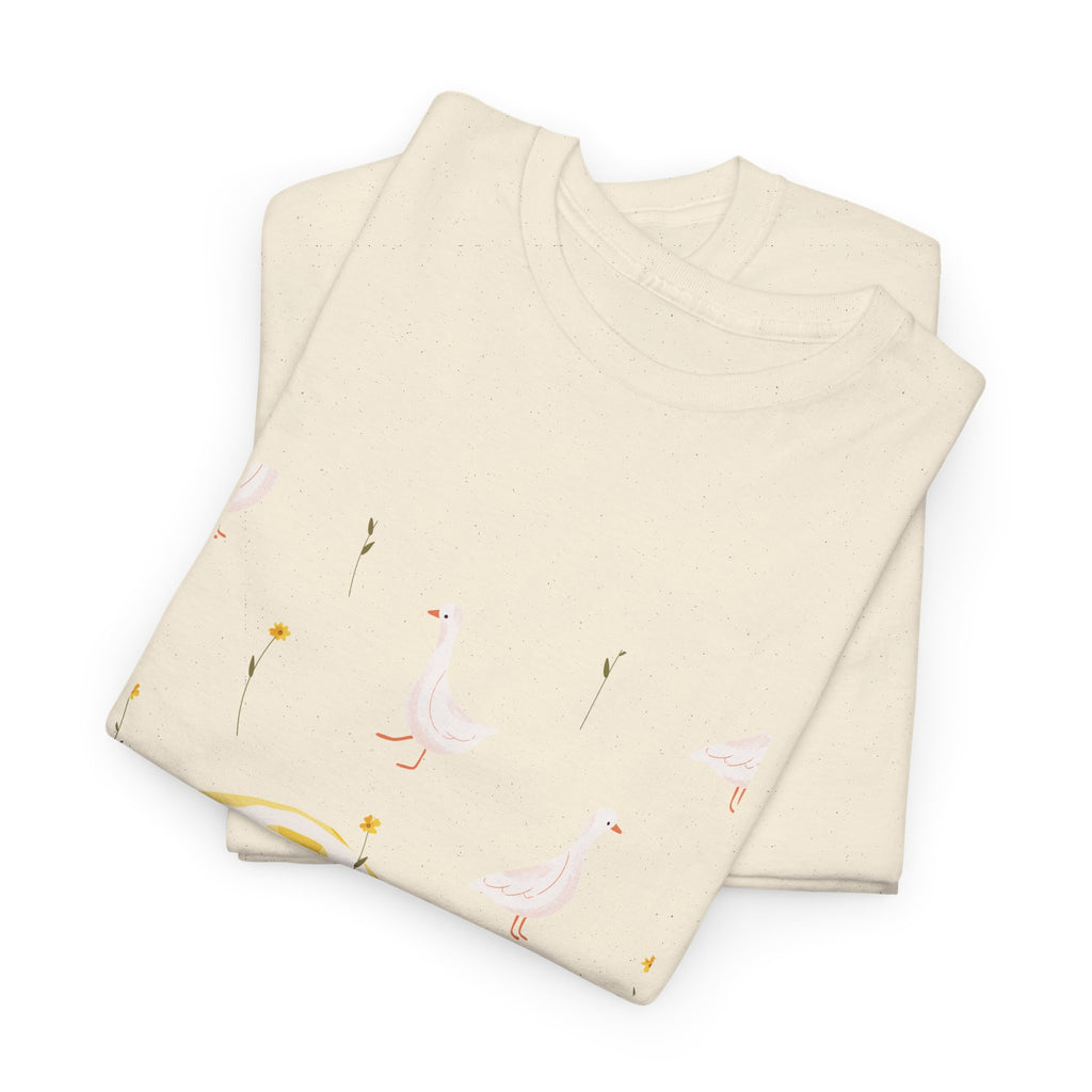 A folded beige t-shirt featuring a graphic design of white ducks all over, with a juicy lemon in the bottom-left corner.