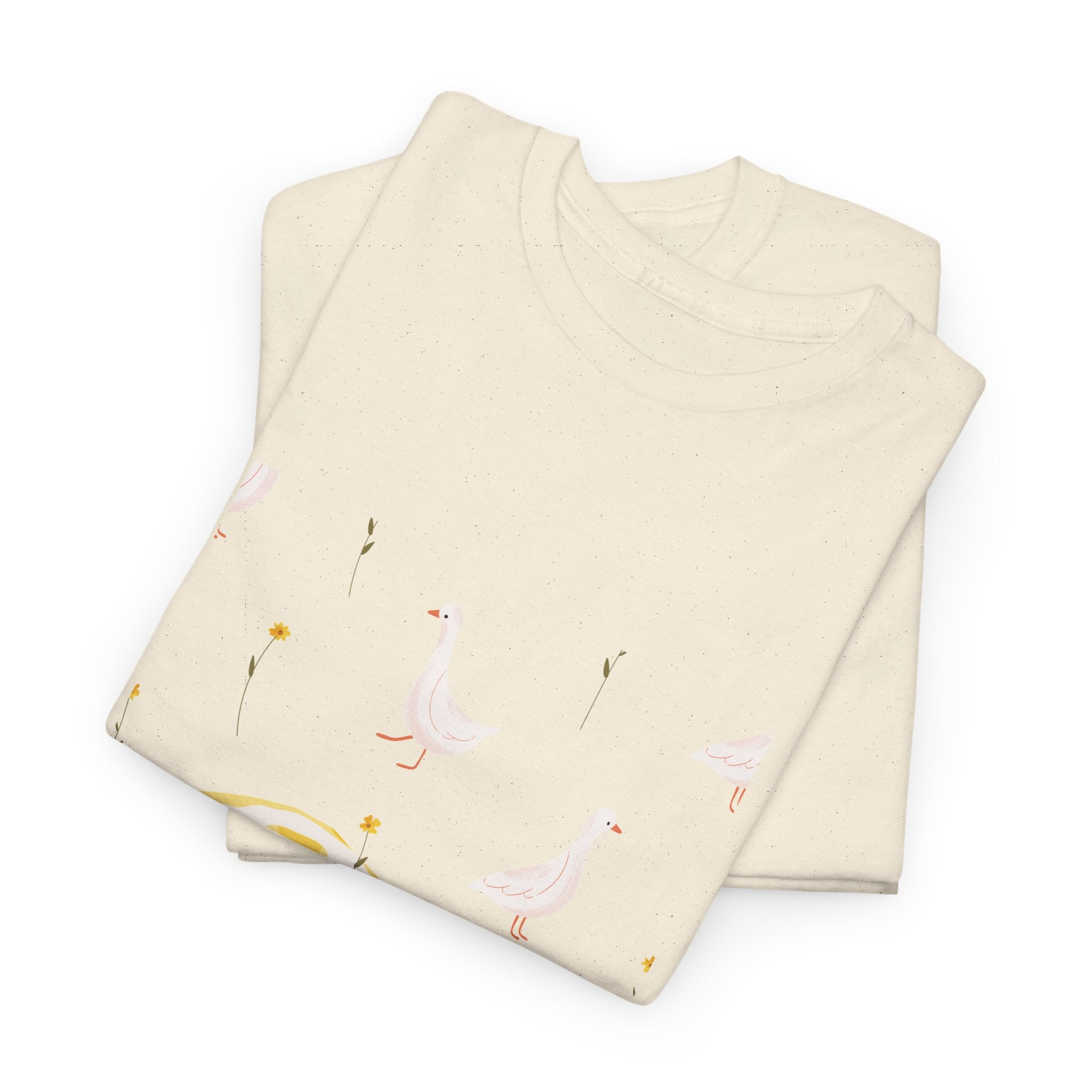 A folded beige t-shirt featuring a graphic design of white ducks all over, with a juicy lemon in the bottom-left corner.