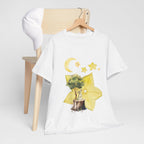 A white t-shirt hanging on a chair, featuring a graphic design of a tree stump, leaves, and starfruit celestial elements.