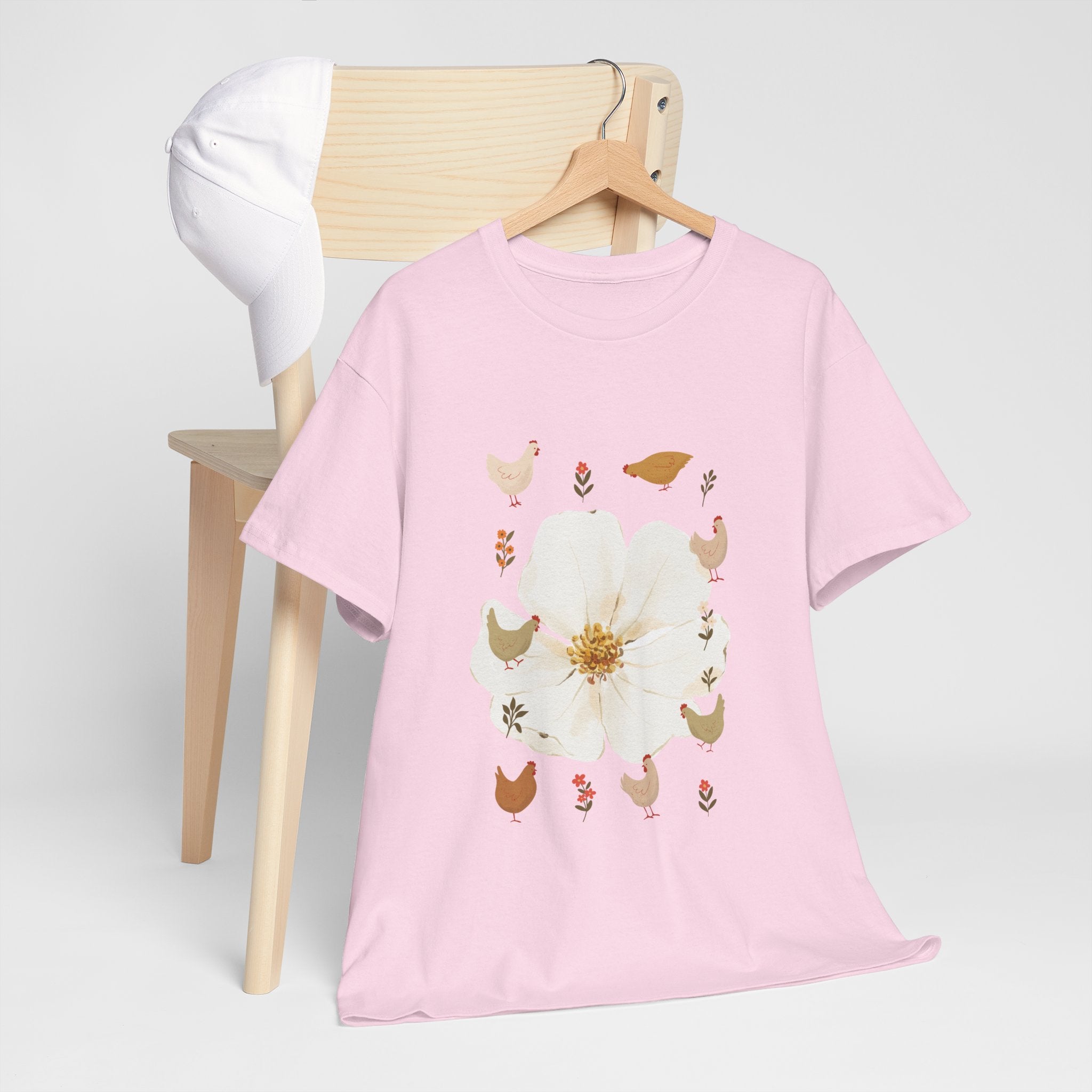 A pink t-shirt hanging on a chair, featuring a graphic design of a bloom surrounded by roosters in various poses.