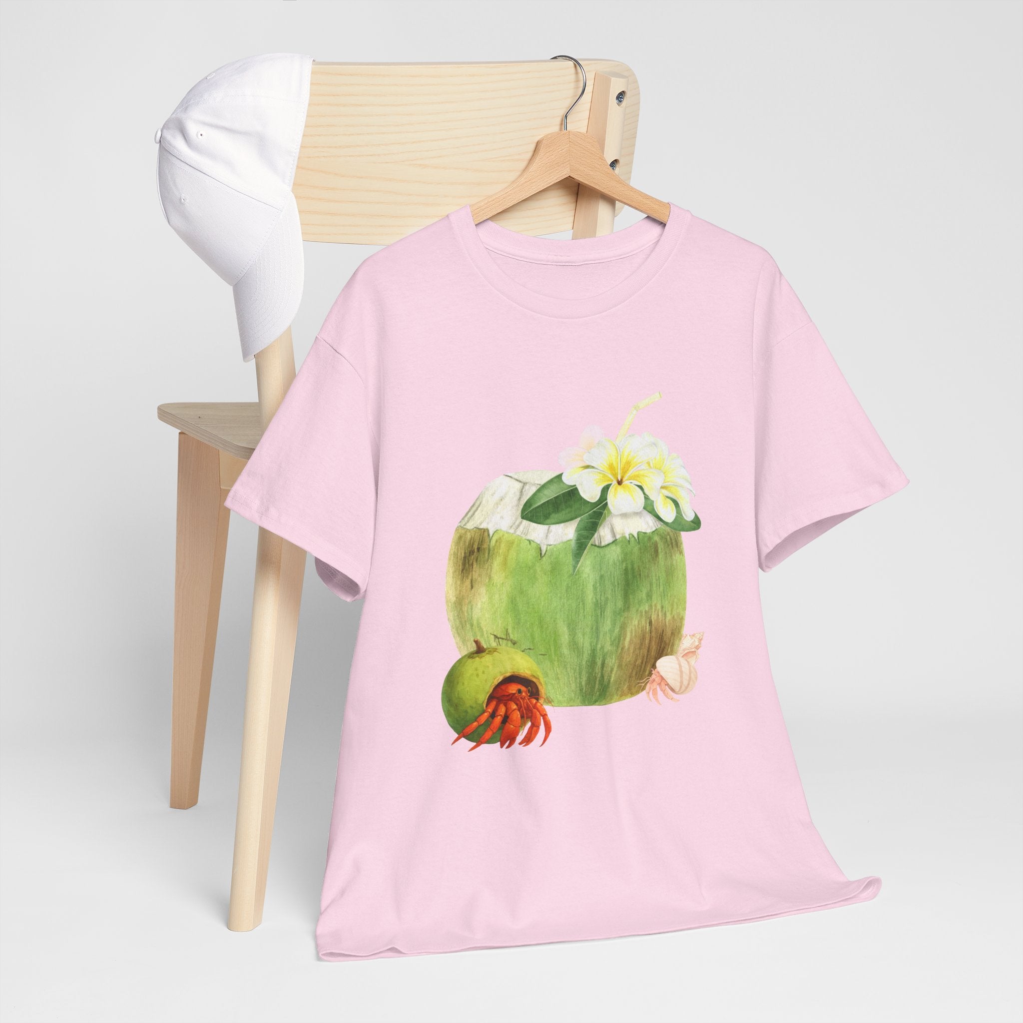 A pink t-shirt hanging on a chair, featuring a graphic design of a hermit crab in a coconut shell and a straw-topped coconut.