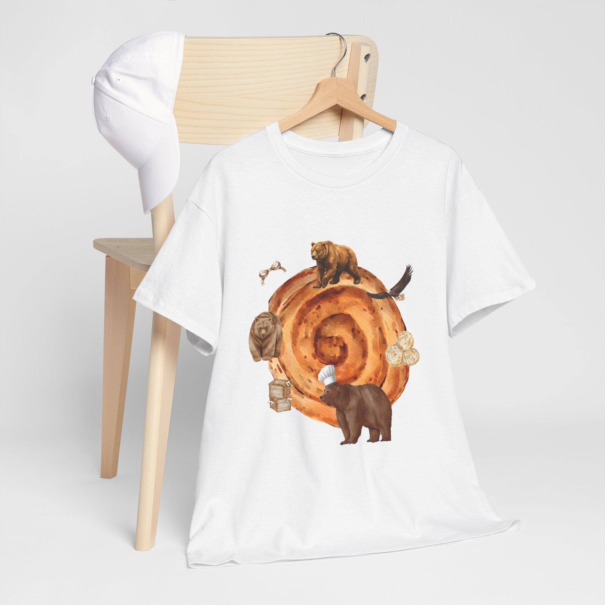 A white t-shirt hanging on a chair, featuring a graphic design of a cinnamon roll surrounded by several hungry bears.