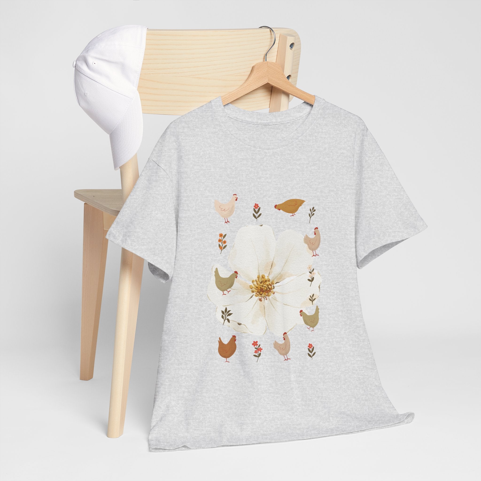 A grey t-shirt hanging on a chair, featuring a graphic design of a bloom surrounded by roosters in various poses.