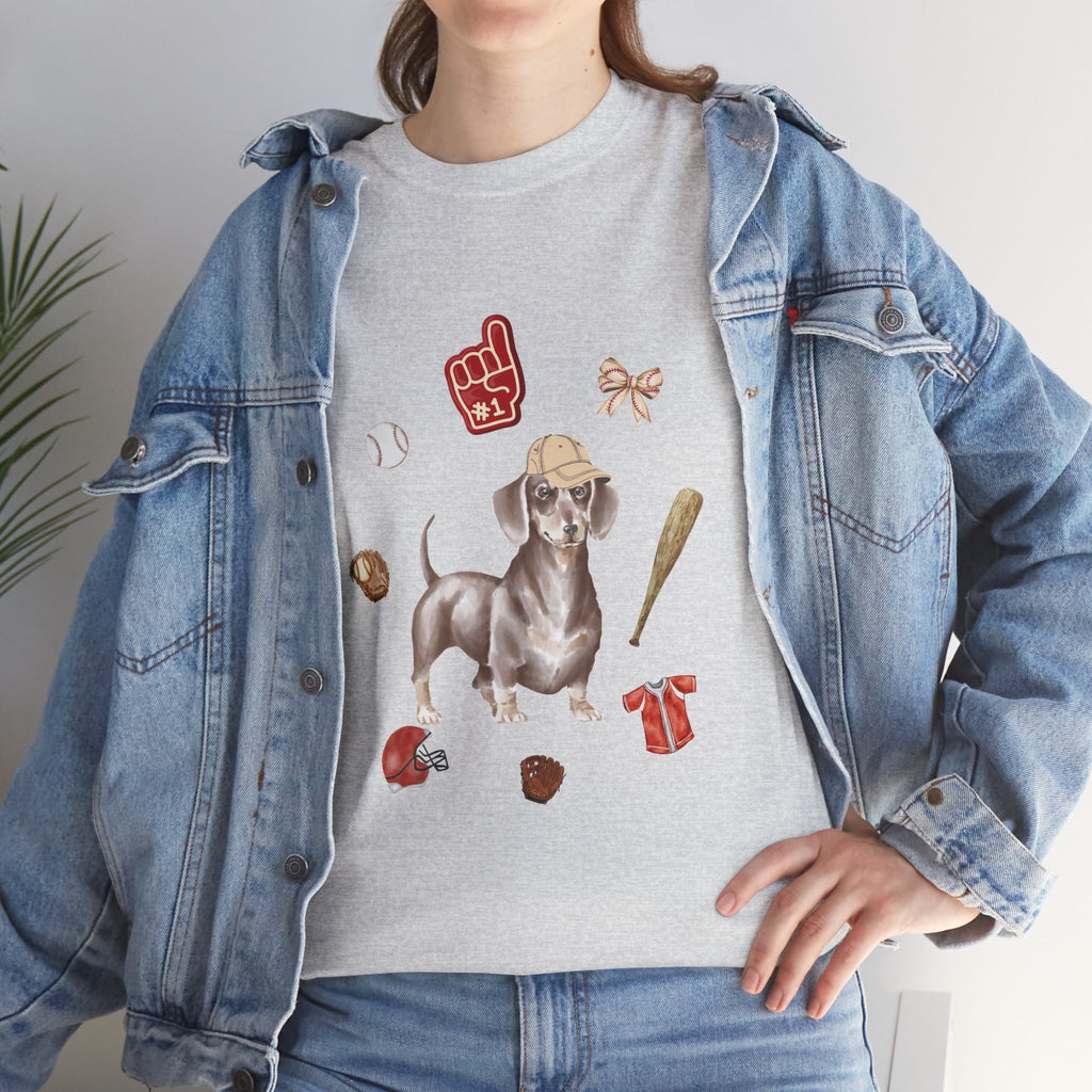A girl wearing a denim jacket over a grey t-shirt featuring a colorful design of a dog in a baseball hat surrounded by a circle of balls, bats, and helmets.
