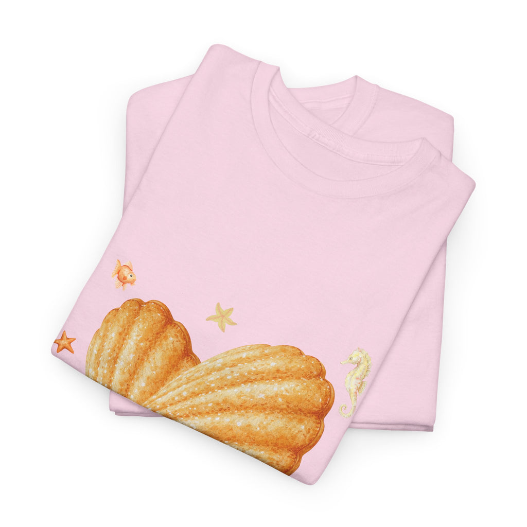 A folded pink t-shirt featuring a graphic design of a heart-shaped madeleine surrounded by yellow tropical fish, starfish, seahorses, and coral.
