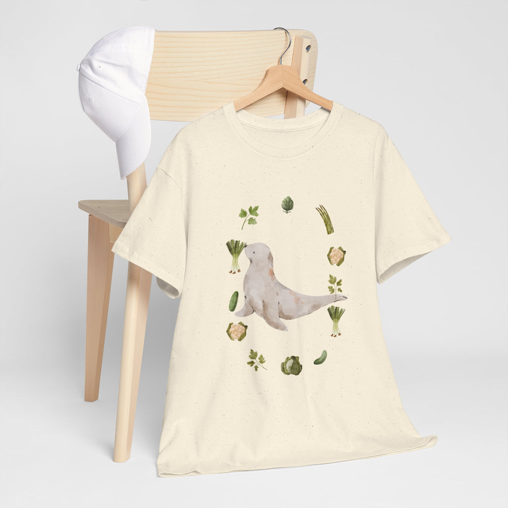A beige t-shirt hanging on a chair, featuring a graphic design of a sea lion surrounded by green onions, cabbage, and broccoli.