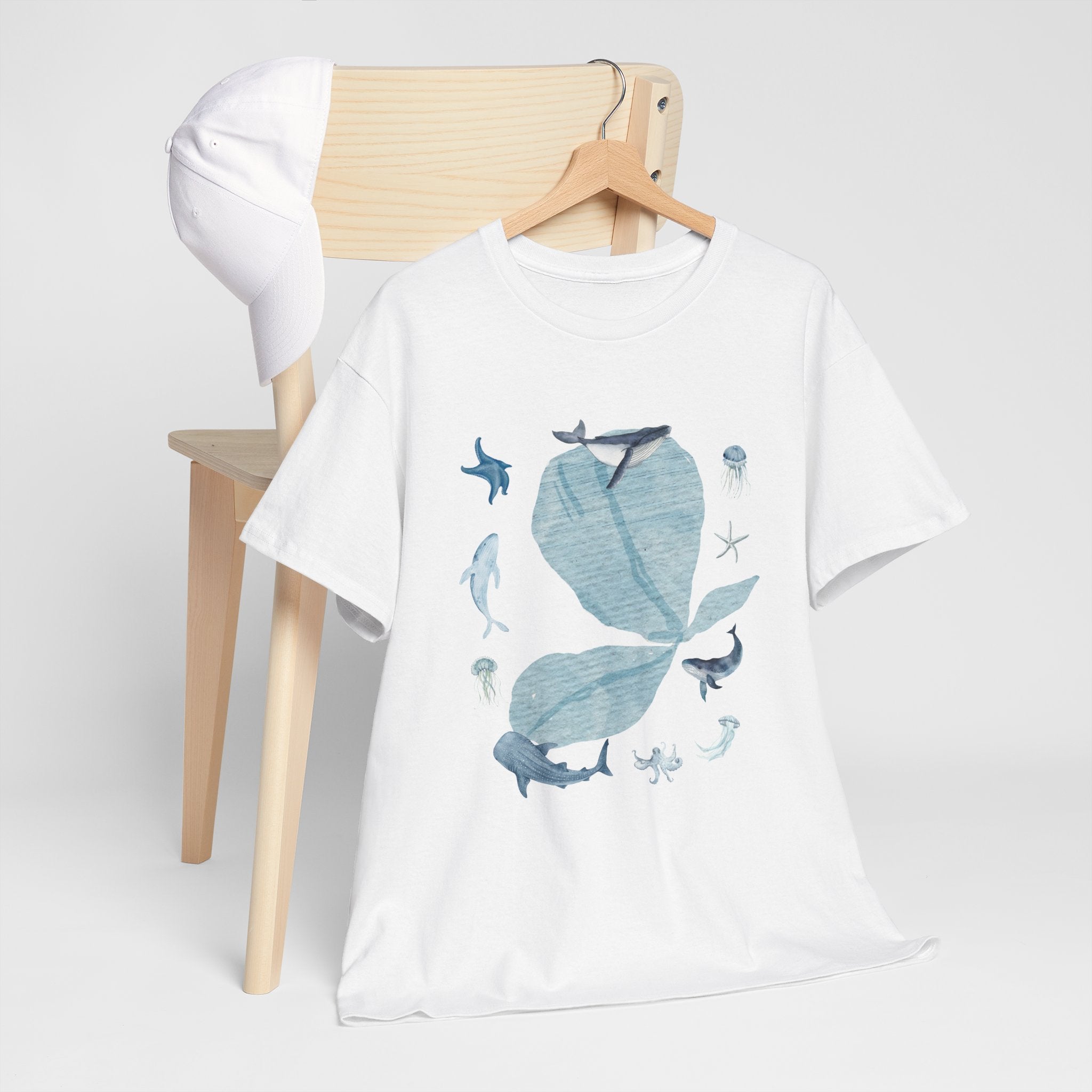 A white t-shirt hanging on a chair, featuring a graphic design of a blue bloom surrounded by whales, jellyfish, and starfish.