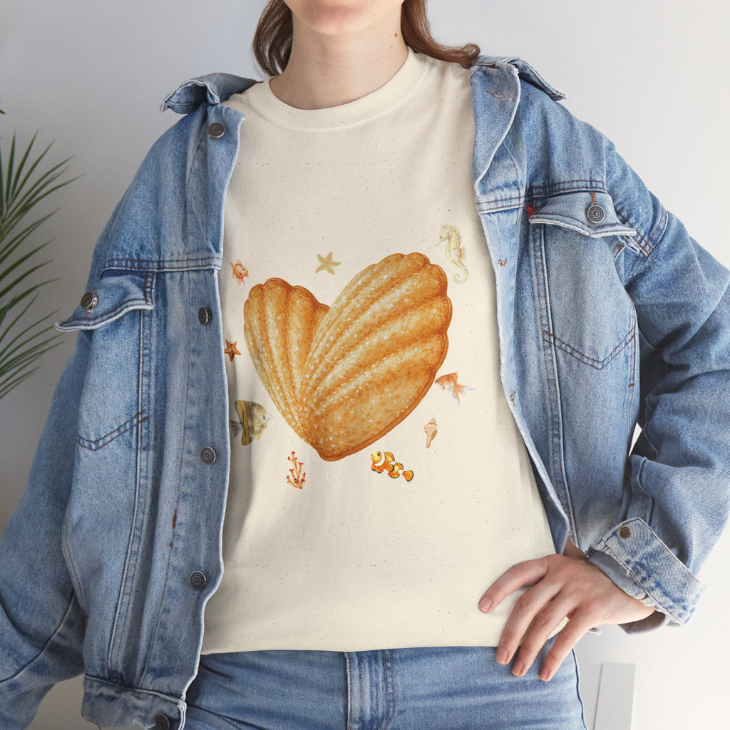 A girl wearing a denim jacket over a beige t-shirt featuring a colorful design of a heart-shaped madeleine surrounded by yellow tropical fish, starfish, seahorses, and coral.
