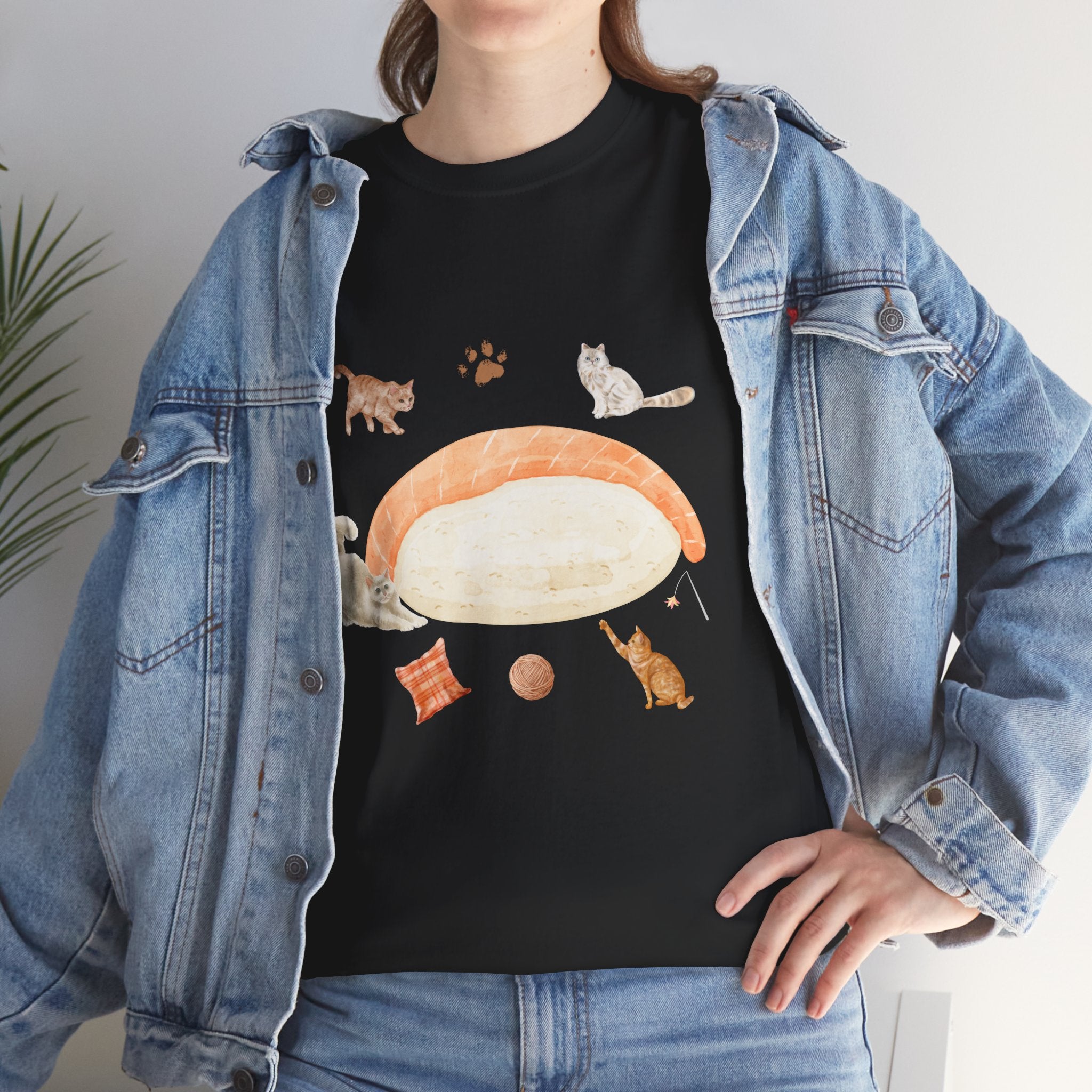 A girl wearing a denim jacket over a black t-shirt featuring a colorful design of a piece of nigiri sushi surrounded by a circle of cats, yarn balls, and cushions.