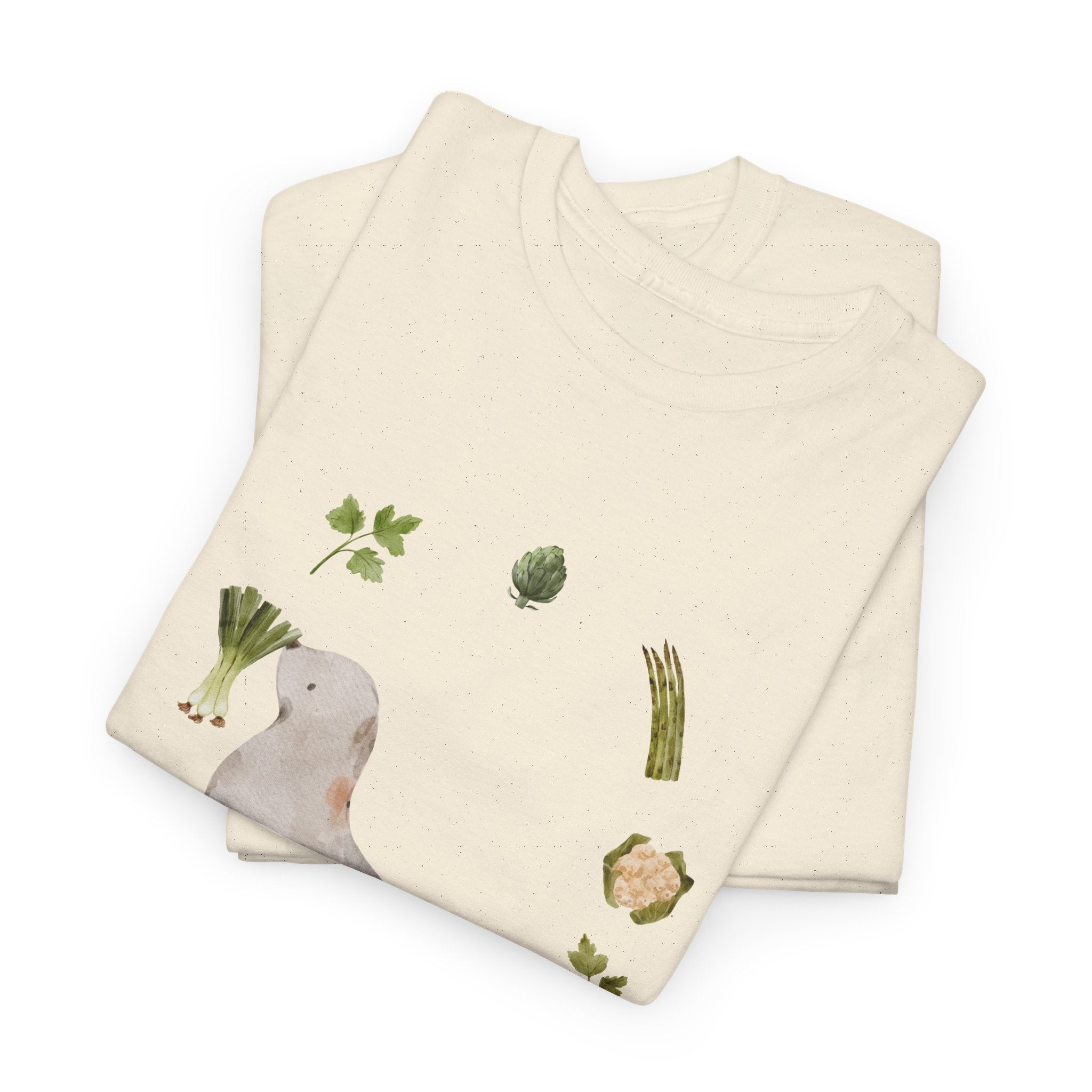 A folded beige t-shirt featuring a graphic design of a sea lion surrounded by green onions, cabbage, and broccoli.