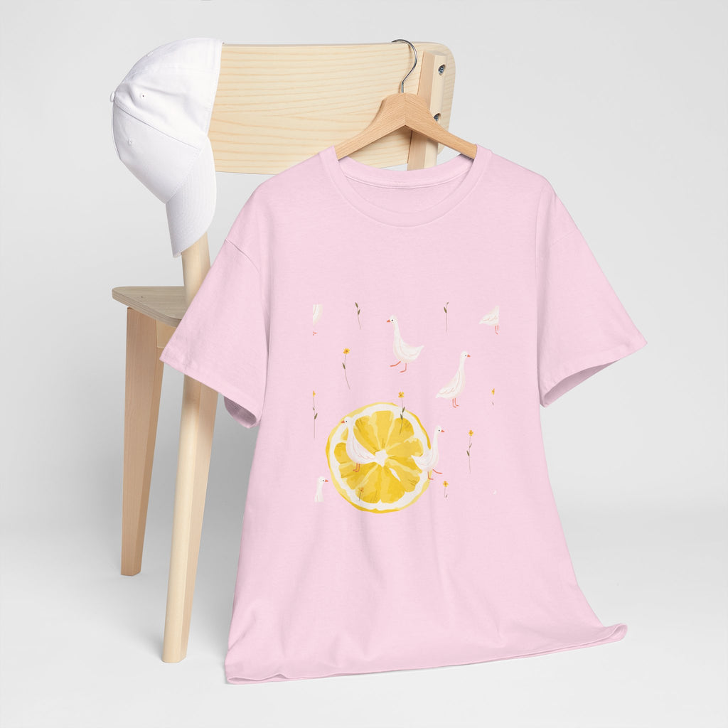 A pink t-shirt hanging on a chair, featuring a graphic design of white ducks across the whole shirt and a juicy lemon in the bottom-left corner.