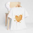 A white t-shirt hanging on a chair, featuring a graphic design of a heart-shaped madeleine surrounded by yellow tropical fish, starfish, seahorses, and coral.