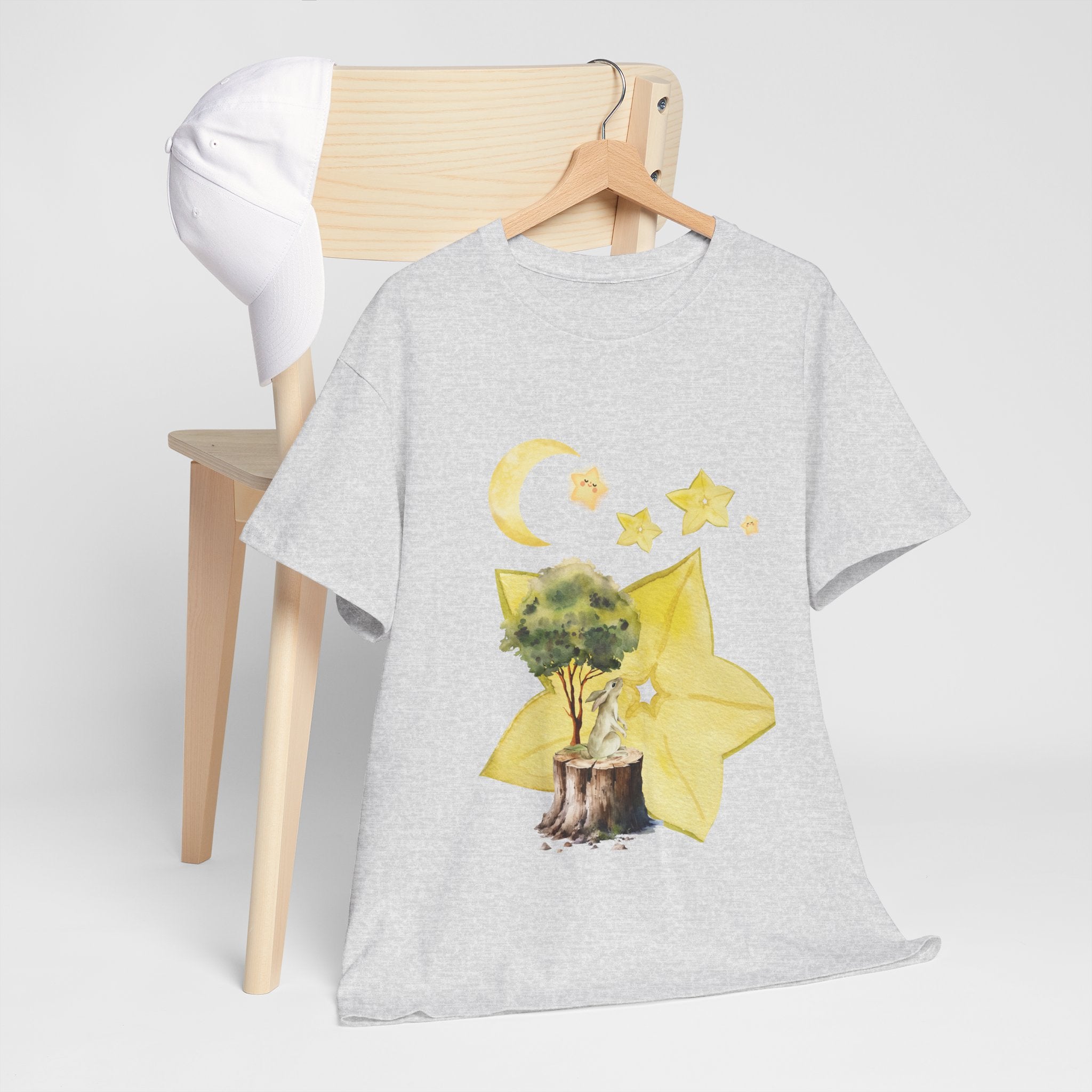 A grey t-shirt hanging on a chair, featuring a graphic design of a tree stump, leaves, and starfruit celestial elements.