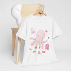 A white t-shirt hanging on a chair, featuring a graphic design of a pink octopus multitasking its tentacles to apply lipstick, brush on makeup, and juggle beauty accessories.