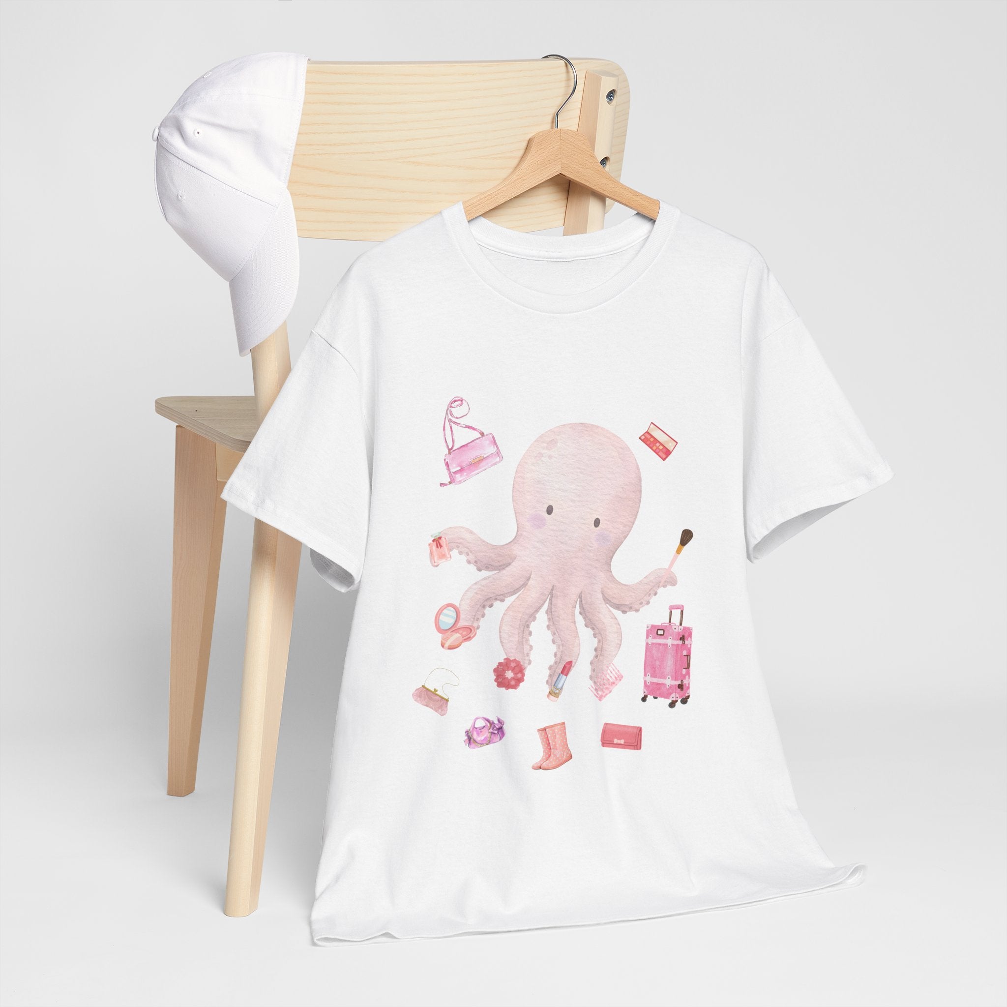 A white t-shirt hanging on a chair, featuring a graphic design of a pink octopus multitasking its tentacles to apply lipstick, brush on makeup, and juggle beauty accessories.