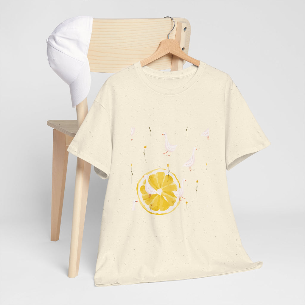 A beige t-shirt hanging on a chair, featuring a graphic design of white ducks across the whole shirt and a juicy lemon in the bottom-left corner.
