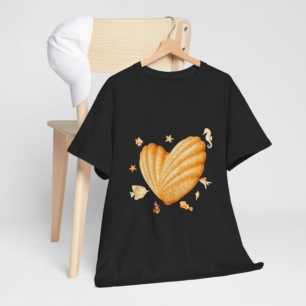 A black t-shirt hanging on a chair, featuring a graphic design of a heart-shaped madeleine surrounded by yellow tropical fish, starfish, seahorses, and coral.