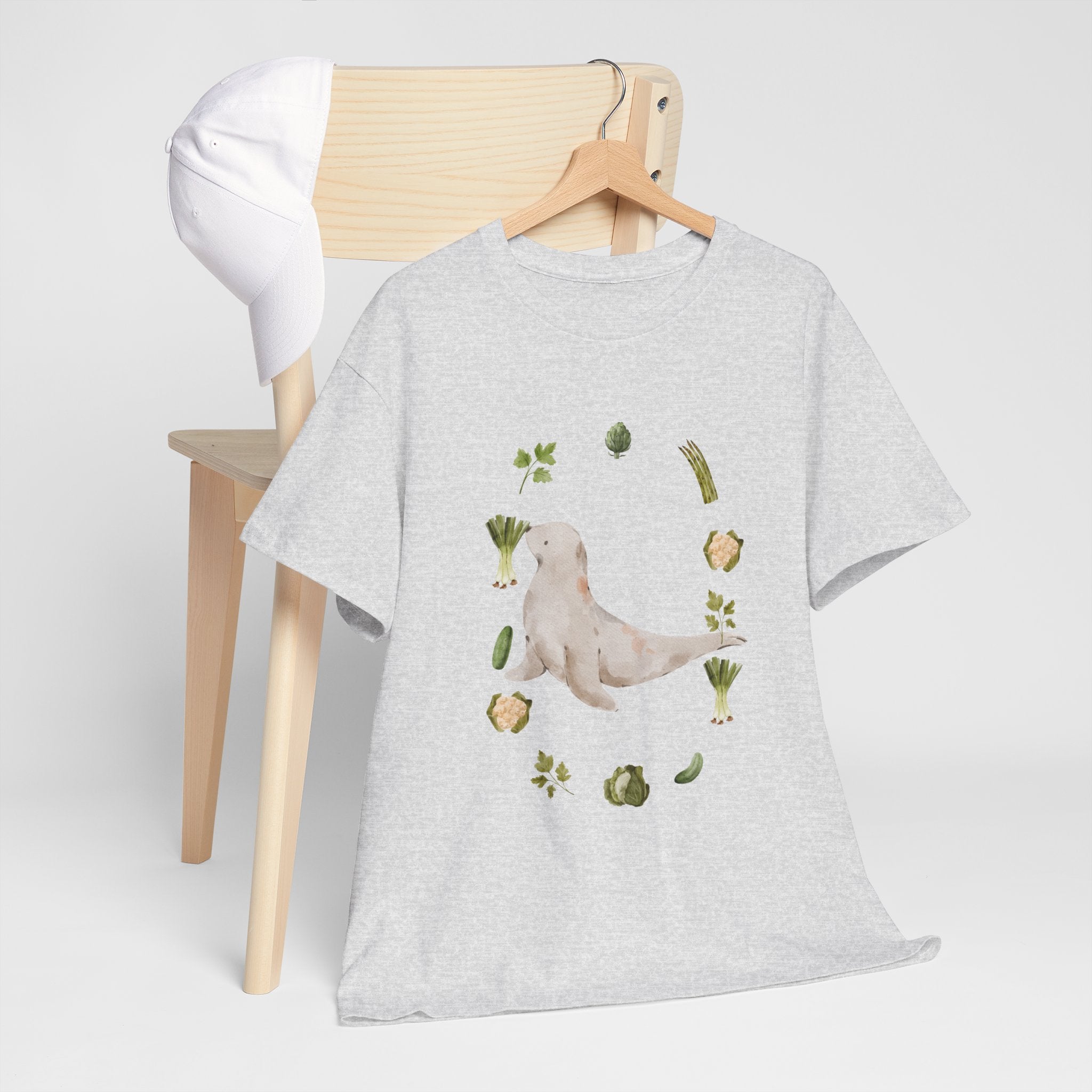 A grey t-shirt hanging on a chair, featuring a graphic design of a sea lion surrounded by green onions, cabbage, and broccoli.