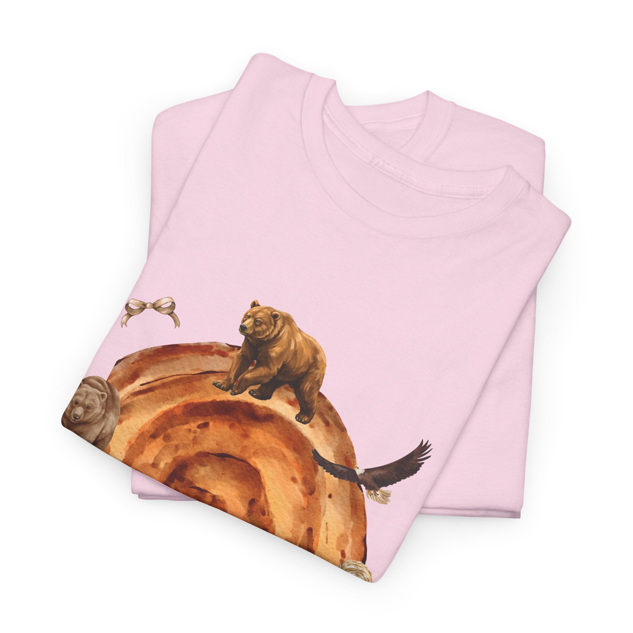 A folded pink t-shirt featuring a graphic design of a cinnamon roll surrounded by several hungry bears.
