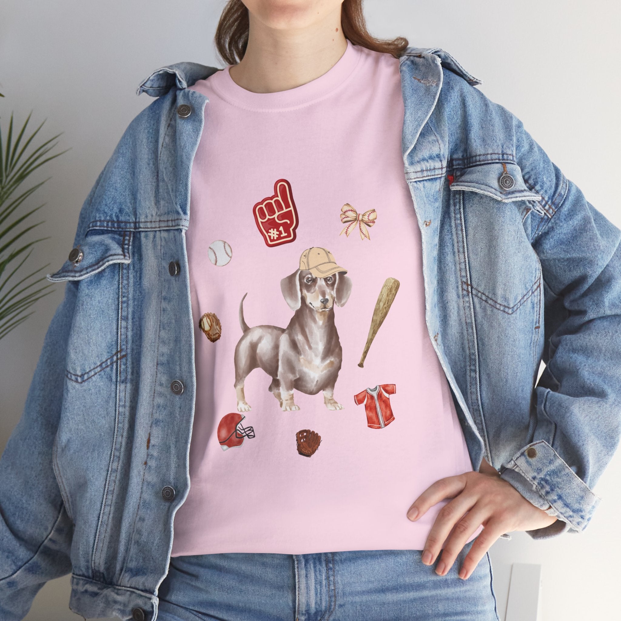 A girl wearing a denim jacket over a pink t-shirt featuring a colorful design of a dog in a baseball hat surrounded by a circle of balls, bats, and helmets.