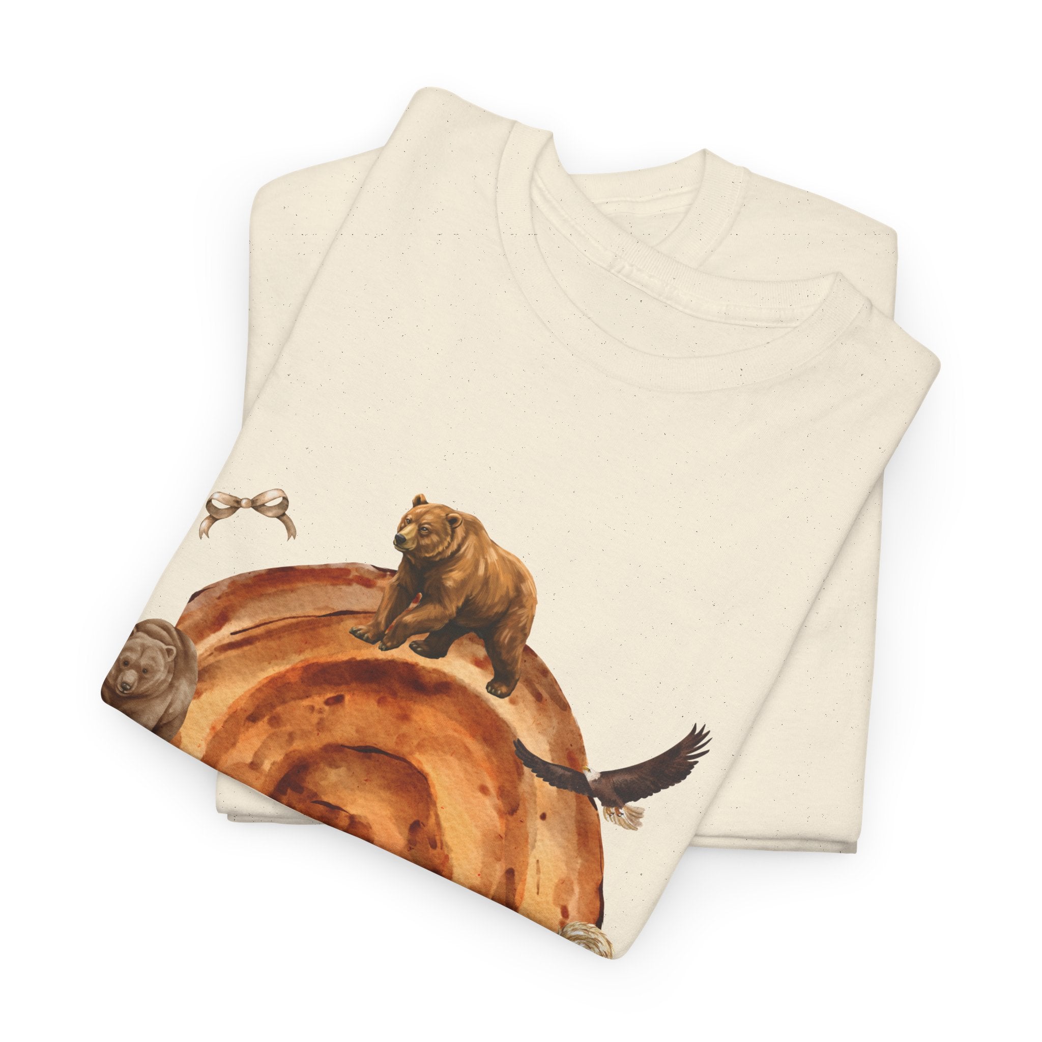 A folded beige t-shirt featuring a graphic design of a cinnamon roll surrounded by several hungry bears.